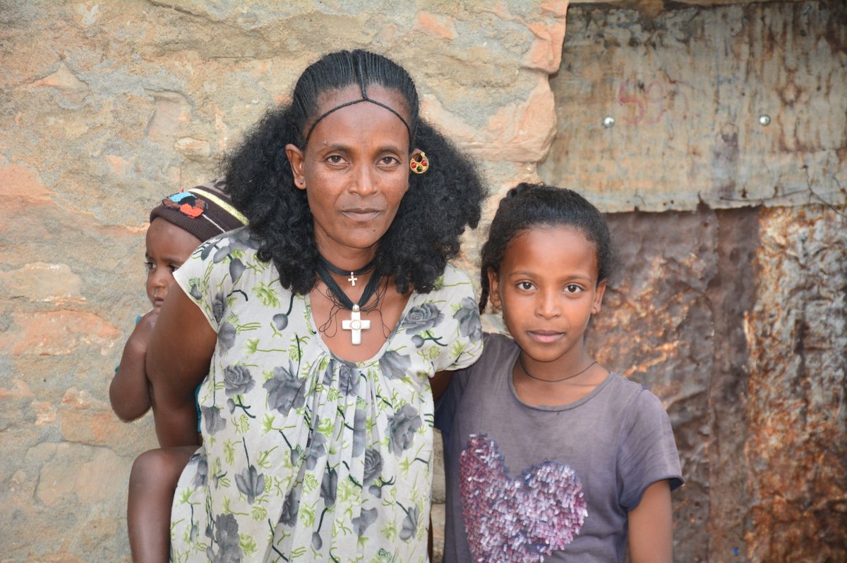 Kvinde med to børn - en på ryggen, en ved siden af.