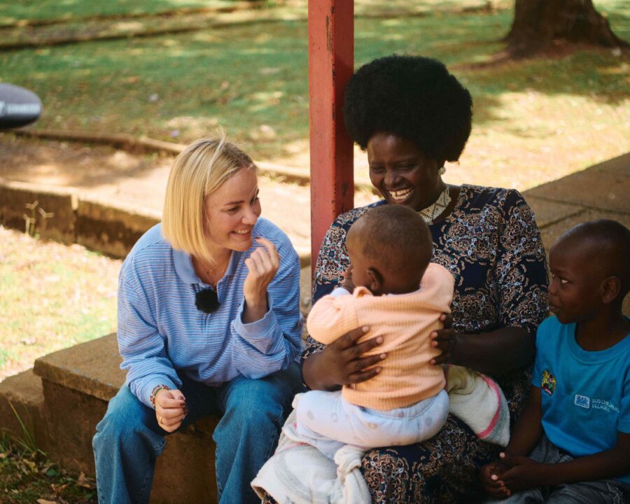 To kvinder og to børn sidder på en veranda. Den ene kvinde har det ene barn på skødet.