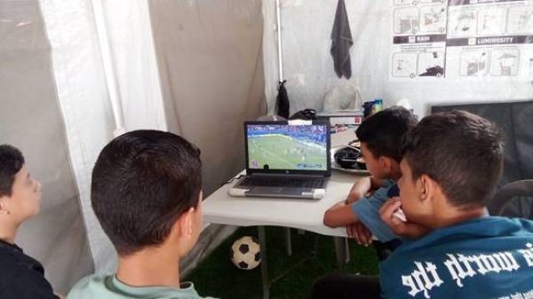 Fire drenge sidder og ser fodbold på en computer i et telt i Gaza